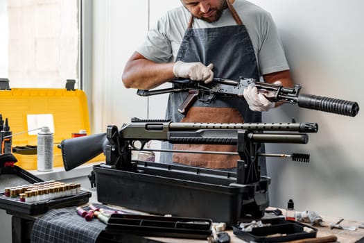 Close up of young man in apron disassembling a gun above the table in a workshop