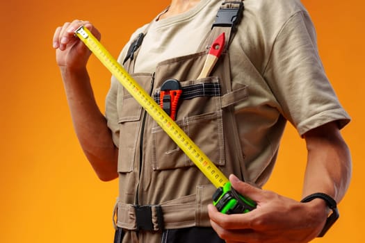 Close up photo of builder holding measuring roulette against yellow background in studio