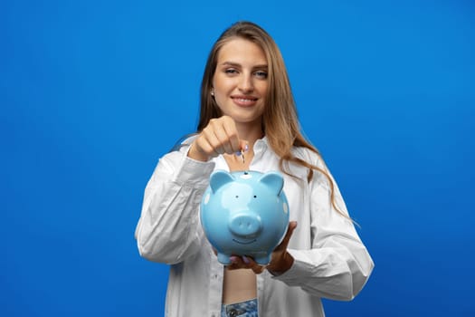 Young caucasian woman holding a piggy bank.against blue background in studio