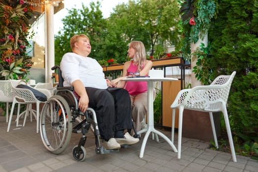 Woman with disability sitting in a wheelchair in outdoor cafe with her young daughter together