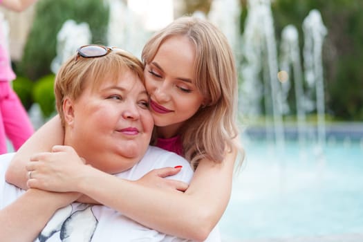 Positive young woman and her mother embracing on city street close up