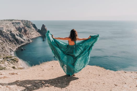 Woman green dress sea. Female dancer posing on a rocky outcrop high above the sea. Girl on the nature on blue sky background. Fashion photo