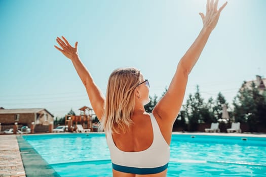 A woman is sitting in a pool with her arms raised in the air. Scene is joyful and carefree