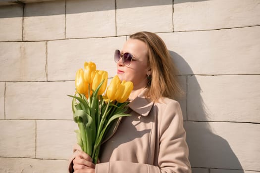 Woman holding yellow tulips, leaning against stone wall. Women's holiday concept, giving flowers