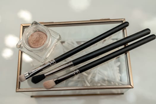 A small box with three makeup brushes and a jar of powder.