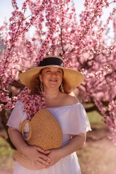 Woman blooming peach orchard. Against the backdrop of a picturesque peach orchard, a woman in a long white dress and hat enjoys a peaceful walk in the park, surrounded by the beauty of nature