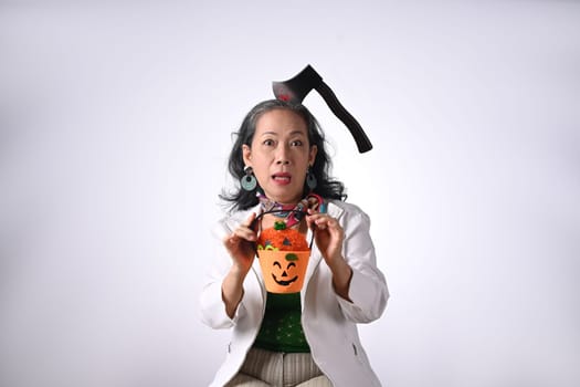 Happy senior woman dressed in halloween costume holding a pumpkin on white background.