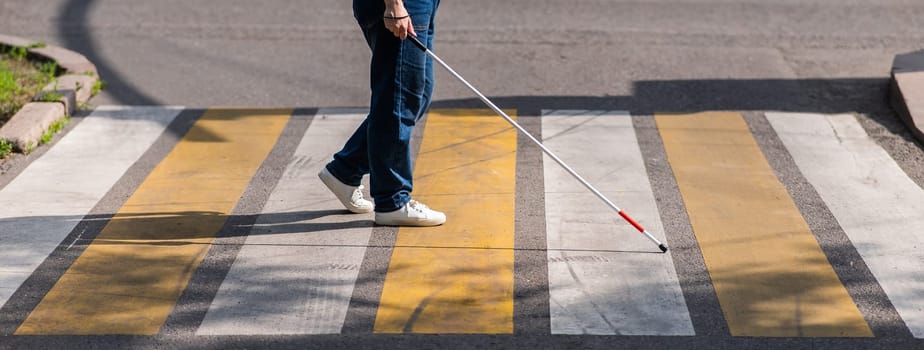 Close-up of the legs of a blind woman crossing the road at a crosswalk with a cane