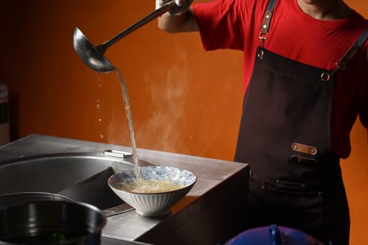 Shot of male chef using a ladle pouring soup into noodle bowl. Thai noodles soup.