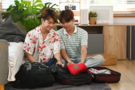 Happy young male couple packing suitcase on floor at home. Travel and vacations concept.
