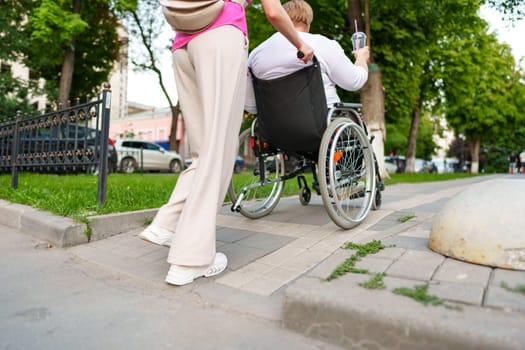 Back view of young woman helping mature woman in wheelchair strolling in the city