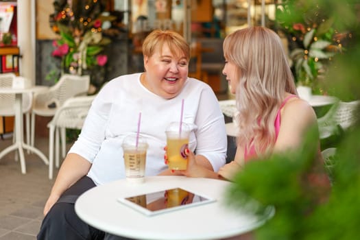 Young daughter and her mother in wheelchair sitting at the table in cafe with drinks and having fun, close up