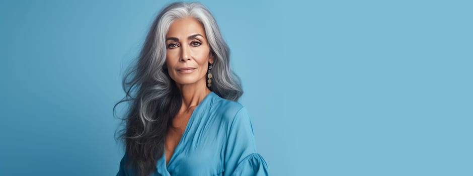Elegant, elderly, chic Latino, Spain woman with gray long hair and perfect skin, on a blue background, banner. Advertising of cosmetic products, spa treatments, shampoos and hair care products, dentistry and medicine, perfumes and cosmetology women