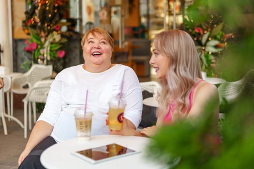 Young daughter and her mother in wheelchair sitting at the table in cafe with drinks and having fun, close up