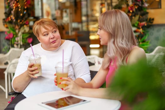 Young daughter and her mother in wheelchair sitting at the table in cafe with drinks and having fun, close up