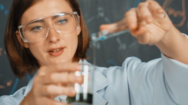 Closeup of young beautiful teacher focus on mixing chemical liquid at laboratory. Skilled scientist doing an experiment by inspect colored solution while standing in front of blackboard. Erudition.