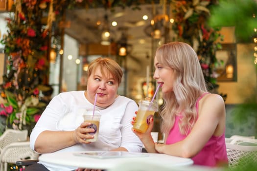 Young daughter and her mother in wheelchair sitting at the table in cafe with drinks and having fun, close up