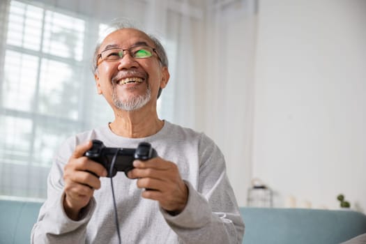 Asian mature man hands using game controller play videogame, Funny on retirement elderly smile sitting on sofa life gaming, senior old man enjoying holding joystick playing video game at home
