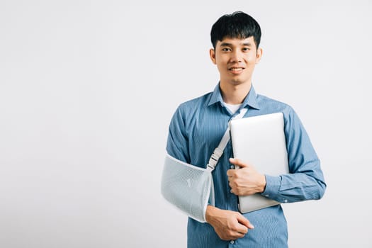 Despite a broken arm, a dedicated business man works with a laptop, supported by a splint. Studio shot isolated on white, highlighting resilience and recovery. Copy space is featured.