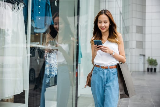 Woman with a smartphone in her hand, standing in front of a wall. She is using her device to stay connected to the digital age, enjoying the entertainment and distraction it offers.