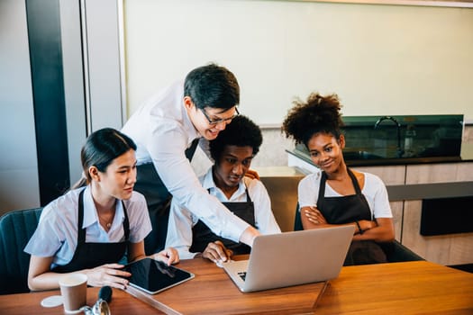 Diverse entrepreneurs hold team meeting in stylish coffee shop. Barista and owner discuss work on laptop. Multiethnic restaurant employees teamwork successful business discussion.