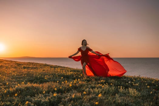 woman red dress is standing on a grassy hill overlooking the ocean. The sky is a beautiful mix of orange and pink hues, creating a serene and romantic atmosphere