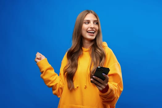 Portrait of young beautiful woman texting on the phone against blue background in studio