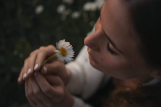 A woman is holding a white flower in her hand. The flower is a daisy, and it is a close-up of the woman's face. Concept of calm and serenity