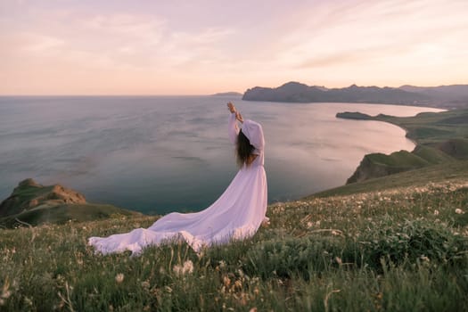 A woman in a white dress stands on a grassy hill overlooking the ocean. The scene is serene and peaceful, with the woman's pose and the beautiful landscape creating a sense of calm and tranquility