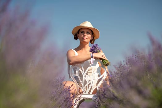 A woman is sitting in a field of lavender flowers and wearing a straw hat. She is smiling and holding a bouquet of flowers. Scene is peaceful and serene, as the woman is surrounded by the beauty of nature.