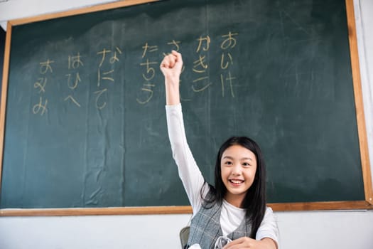 A girl is holding her hand up in the air in front of a blackboard with writing in Chinese