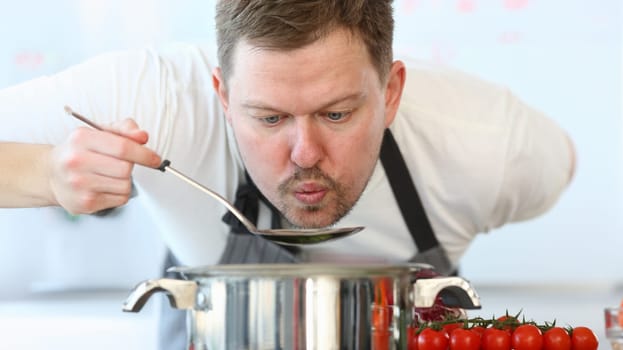 Professional Chef Blowing Soup Ladle Photography. Culinary Blog at Home. Man Holding Kitchen Spoon in Hand. Fresh and Red Tomato. Organic Vegetarian Food. Recipe for Vegan. Horizontal Photography.