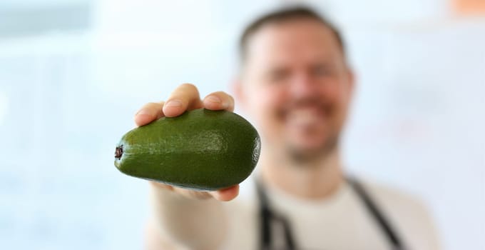 Chef Showing Exotic Green Avocado Photography. Man Holding Ripe Tropical Fruit in Hand. Delicious and Organic Vegetarian Kitchen. Fresh and Healthy Food for Vegan. Fresh Ingredient Partial View Shot