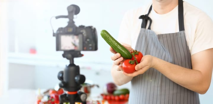 Comic Culinary Blogger Holding Organic Vegetables. Chef Recording Joke with Cucumber and Tomato for Blog on Camera. Man in Apron Showing Ingredient Assortment for Healthy Food Horizontal Shot.