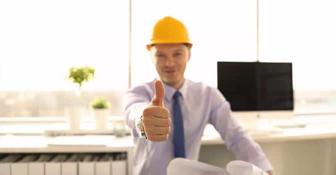 Creative Achitect Working at Engineering Office. Smiling Designer in Yellow Helmet at Workplace Showing Thumb Up Sign Shallow Focus. Project Engineer Approve Project Looking at Camera