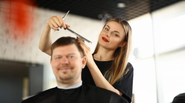 Female Hairdresser Combing Male Client in Salon. Woman Hairstylist Making Hairstyle for Man Sitting in Beauty Studio. Stylist Holding Comb and Scissors for Hair. Girl Styling Haircut for Customer