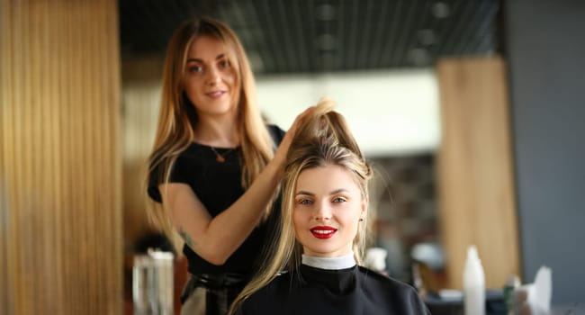 Girl Client Getting Hairstyle by Hairdresser. Hairstylist Holding Hair of Female Customer for Styling New Haircut. Young Beautician Styling Hairdo for Woman with Red Lips Looking at Camera Shot