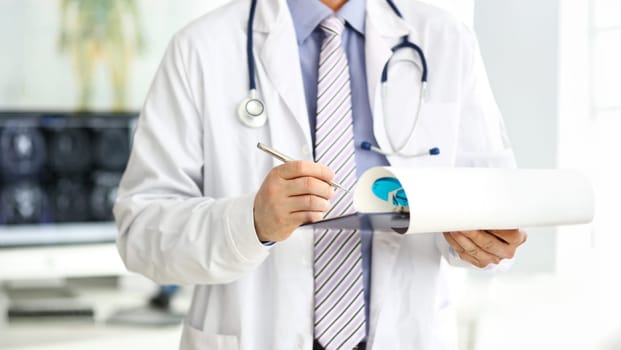 Male doctor checking medical procedure results in document clipped to pad closeup