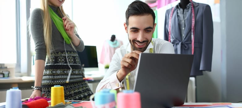 Computer Technology Modern Fashion Sewing Idea. Smiling Man Looking at Laptop Screen. Caucasian Woman Designer Creating Exclusive Garment for Order. People Working at Tailoring Studio