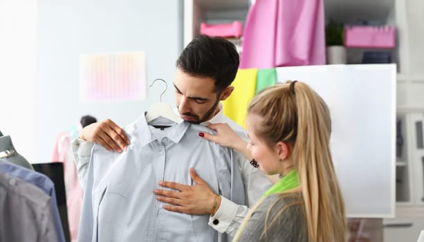 Assistant Buyer Fashion Dressmaker Sewer Service. Caucasian Stylist Standing near Male Purchaser Fitting on Formal Shirt. Girl Designer Consulting about Outfit. Couple at Dressmaking Atelier