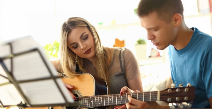 Music Playing Lesson Lovers Couple at Living Room. Caucasian Beautiful People with Acoustic Guitar. Girl Touching Strings, Learning Chords. Professional Performer have Fun Teaching