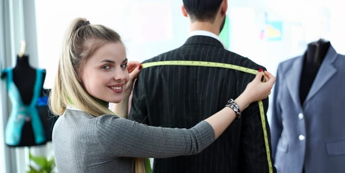 Classy Clothes Design Tailor Craftsmanship Concept. Female Sewer Standing near Male Client Measuring Shoulder Width. Beautiful Woman Taking Measures for Business Suit Using Tape Meter