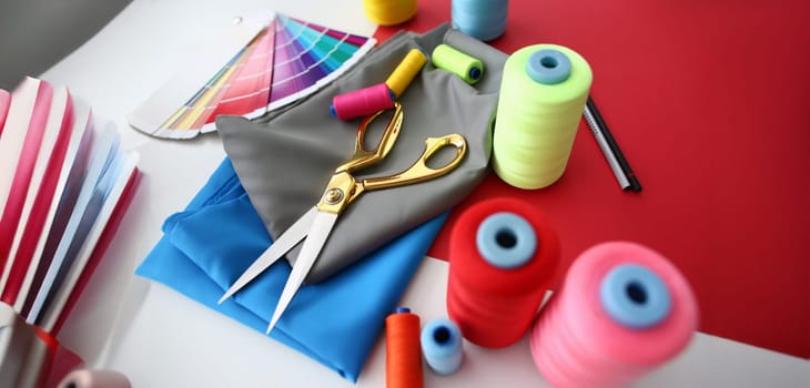 Fashion Designing Tailor Craftsmanship Concept. Fabric, Color Palette and Sewing Tools on Table. Needle Machine Bobbins Spools of Thread with Gold Scissors on Silk Piece. Designer Working Desk