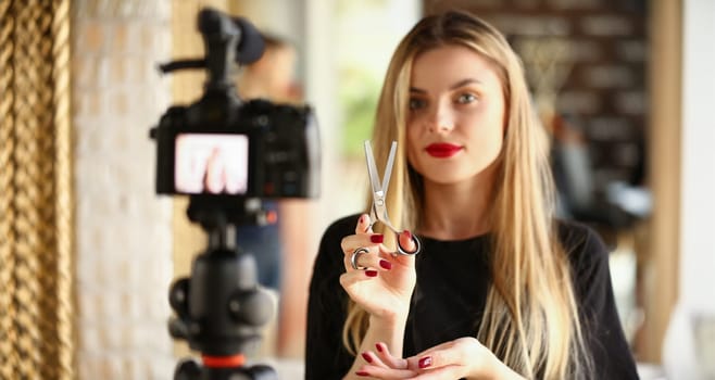 Blonde Woman Blogger Holding Metallic Scissors. Hairdresser Recording Modeling Instrument for Beauty Blog. Hairstylist Showing Cutting Tool on Camera. Girl with Styling Shear Looking at Camera Shot