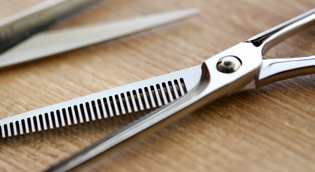 Professional Stainless Scissors Partial View Photo. Stainless Cutting Tool with Comb on Wooden Background. Hairdresser Instrument for Styling Haircut. Sharp Steel Shear Close-up Photography