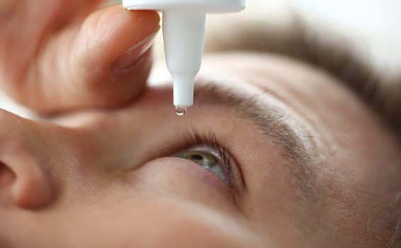 Male hand putting liquid drops in his eye solving vision problem closeup