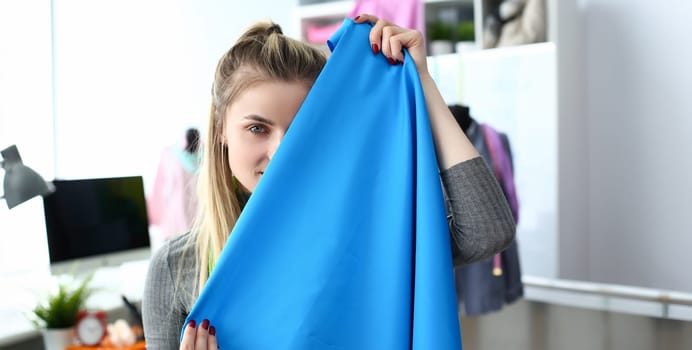 Fashion Clothes Design Fabric Selection Concept. Young Woman Dressmaker Holding Material Sample infront of Face. Caucasian Beautiful Designer Present Textile Piece at Tailor Workshop