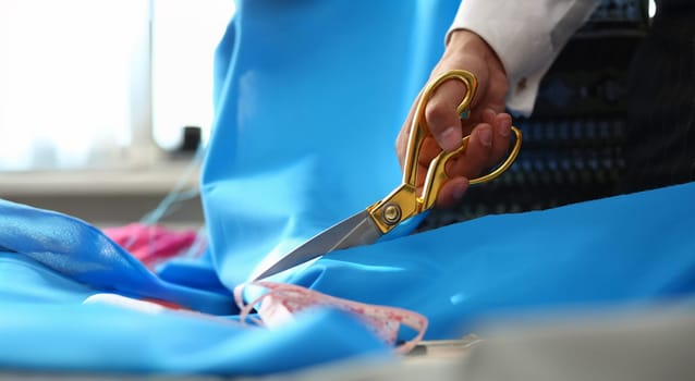 Tailoring Service Dressmaking Process Closeup Shot. Designer Hands Cutting Blue Silky Fabric Using Scissors or Shears. Textile or Fine Cloth Preparing. Sewing Tools on Dressmaker Working Table