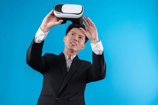 Smiling Asian businessman looking through VR connecting financial business report futuristic metaverse data analytics power bi technology virtual reality meta isolated blue copyspace. Contrivance.