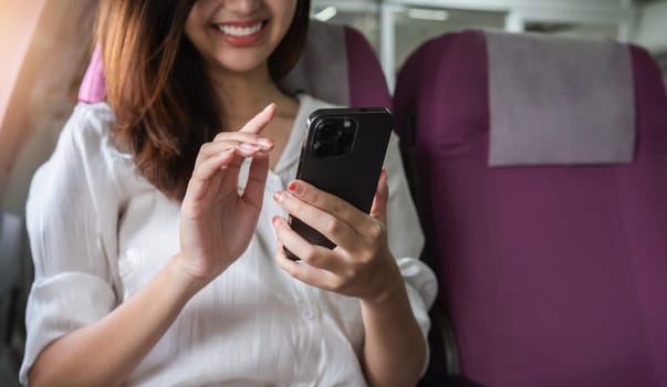 Asian woman using smartphone on airplane seat during flight. Concept of air travel, technology, and connectivity.